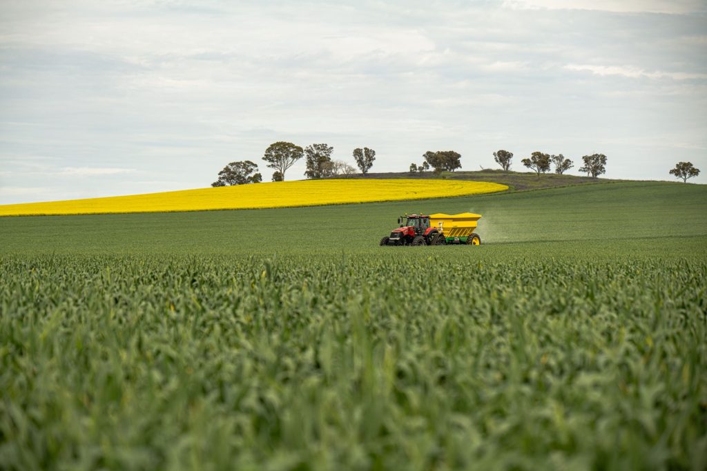 Brasil cria programa para fortalecer indústria nacional de fertilizantes Trator distribui fertilizante sobre uma lavoura verde sob céu nublado.