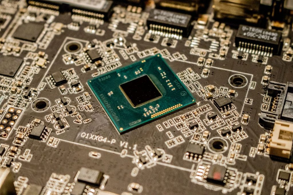 Close de um microchip instalado em uma placa de circuito impresso, rodeado por componentes eletrônicos.