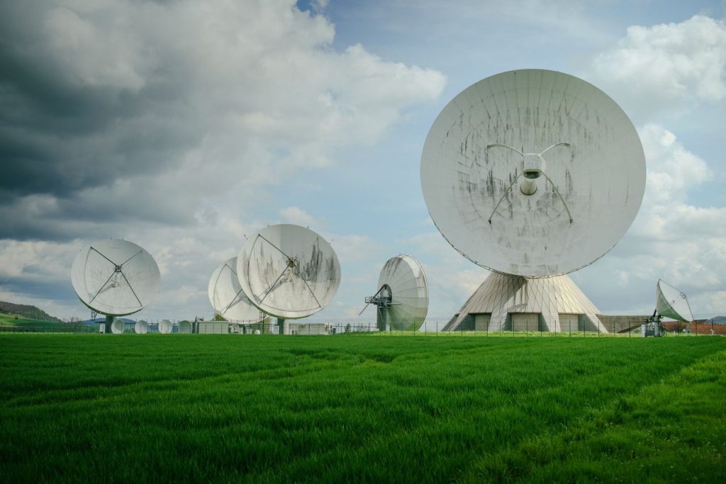 Conjunto de grandes antenas parabólicas instaladas em um campo verde sob céu nublado.