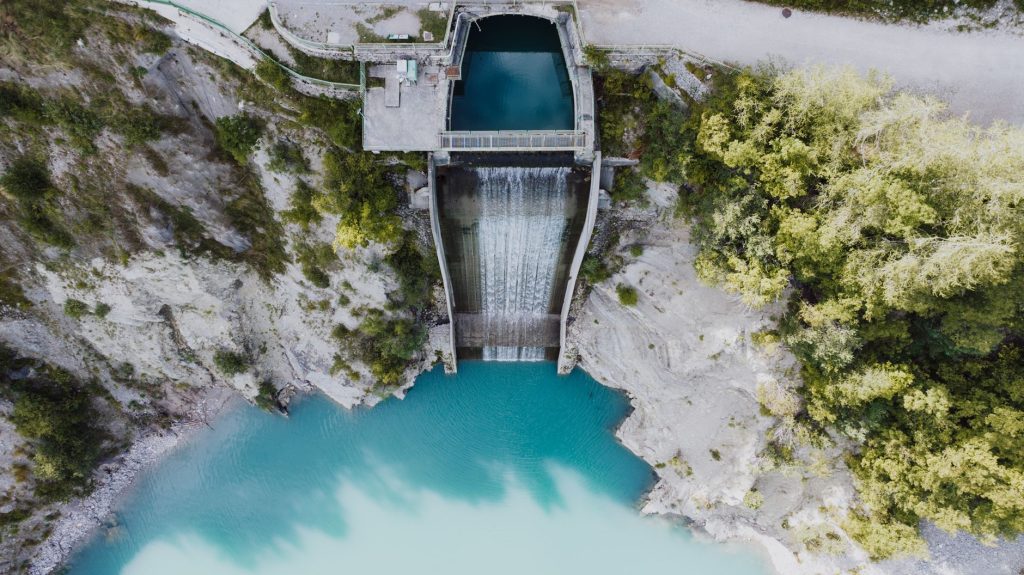 Vista aérea de uma barragem com água azul-turquesa, cercada por áreas naturais.