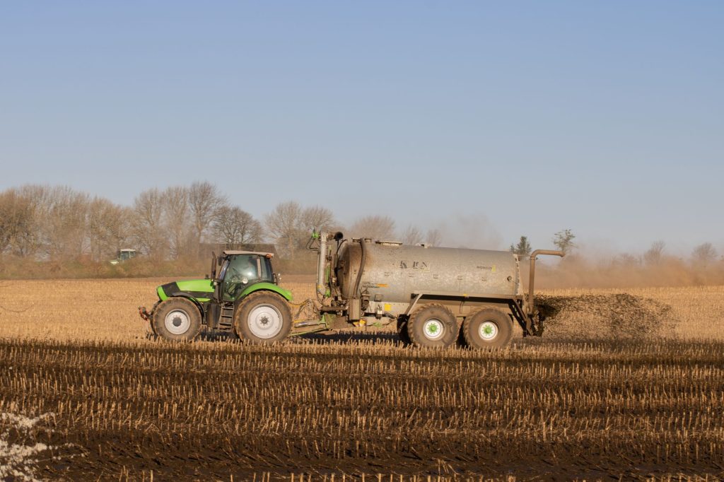 Trator com tanque espalha fertilizante sobre uma área agrícola sob céu claro.